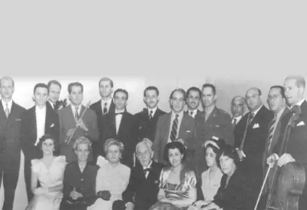 Florent Schmitt recepcionado na ABM, sentado entre Arminda Neves D’Almeida e Cristina Maristany. Em pé alguns acadêmicos (da esquerda para direita): José Vieira Brandão (1º), Alceo Bocchino (6º), Villa-Lobos (8º), Ary Ferreira (12º) e Iberê de Lemos (13º).